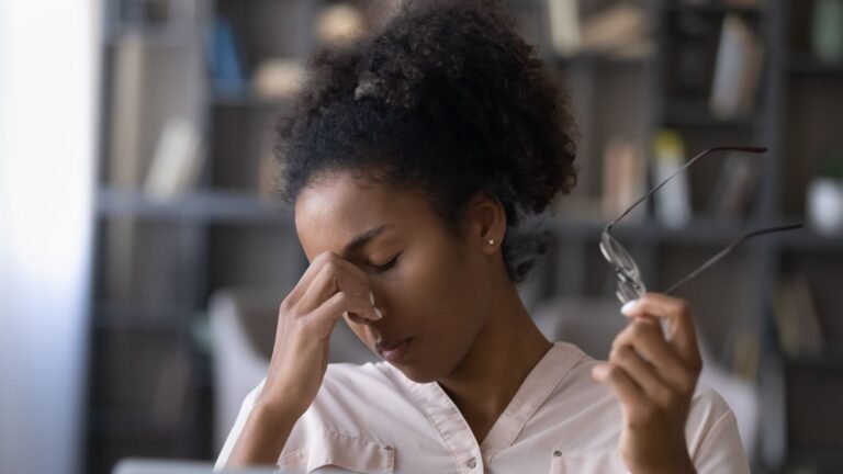 Responsable RH épuisée dans un bureau, se pinçant l’arête du nez avec ses lunettes à la main
