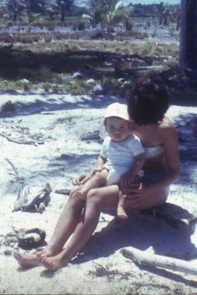 Laurent bébé sur une plage à Tahiti, assis sur les genoux de sa mère