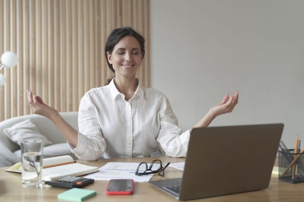 Femme méditant devant un bureau avec un ordinateur portable, pour recentrer son attention en situation de travail.