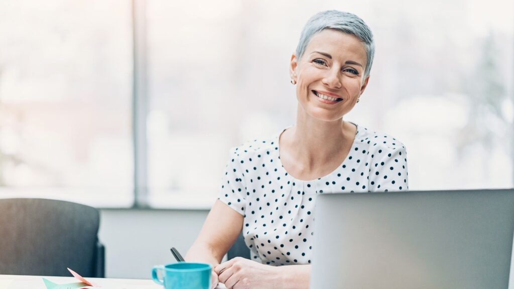 Professionnelle souriante devant son ordinateur dans un bureau lumineux, symbole de renouveau et de sérénité retrouvée.