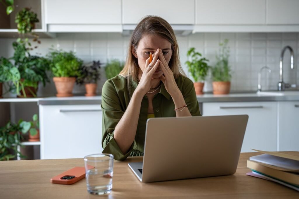 Femme assise devant son ordinateur à la maison, le visage marqué par la fatigue et le stress, illustrant la désorganisation et la pression mentale après une rupture professionnelle.