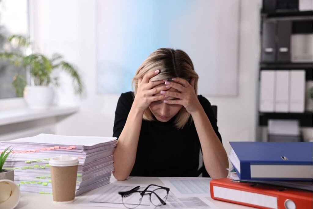 Cadre en surcharge cognitive, entourée de dossiers au bureau, illustrant la pression constante des sollicitations multiples