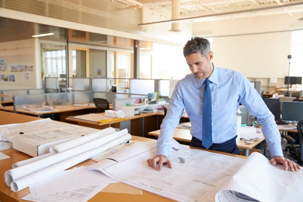 Homme expatrié consultant des plans dans un bureau d’architecture moderne, illustrant les causes professionnelles et organisationnelles de l’isolement à l’étranger
