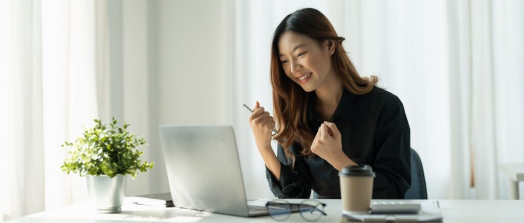 Femme cadre souriante devant son ordinateur après un coaching réussi pour surmonter la charge mentale et retrouver l’équilibre vie pro-vie perso.