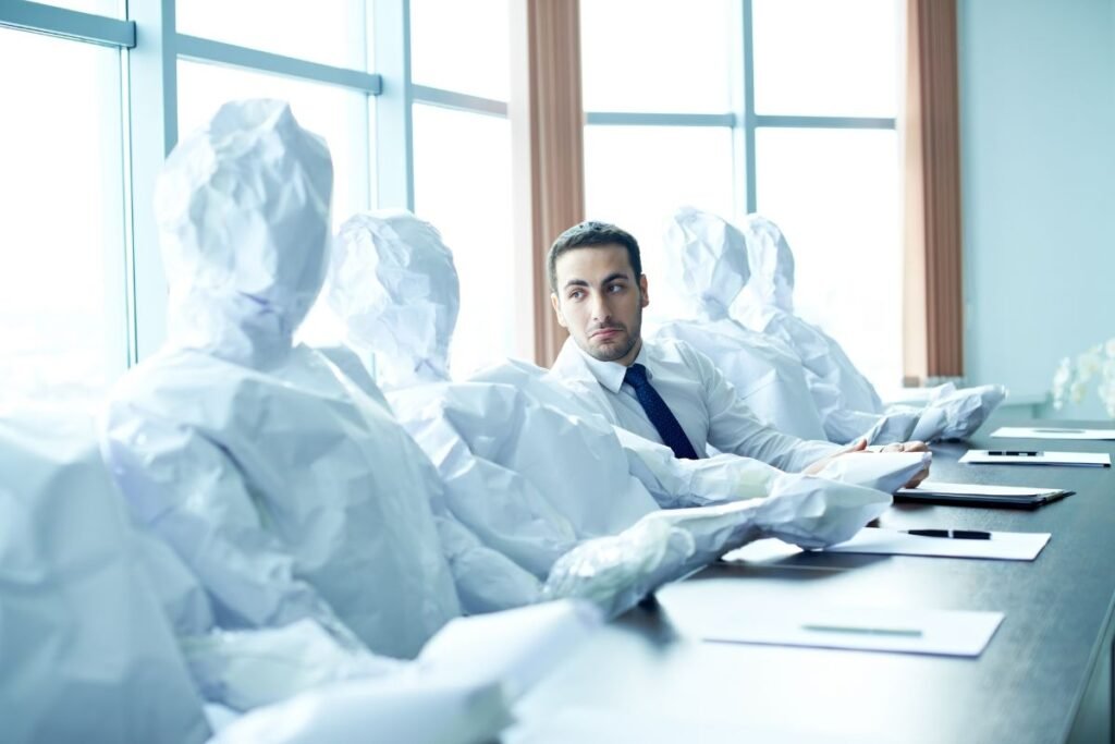 Homme en costume assis seul autour d'une table de réunion, entouré de silhouettes de papier, regard perdu