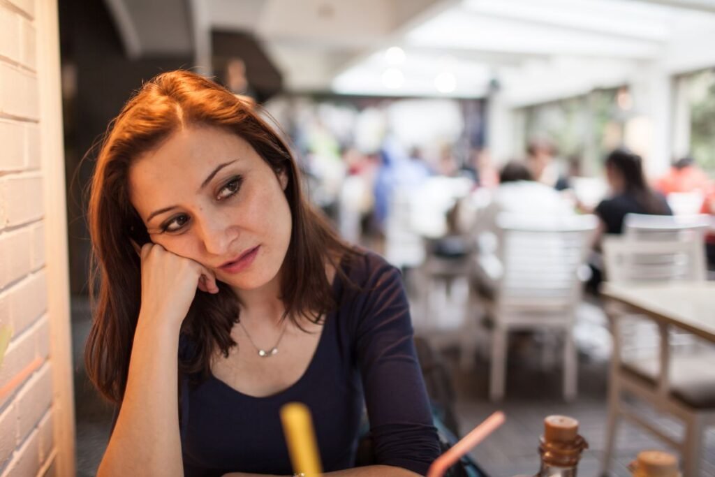 Femme expatriée assise seule dans un café, regard pensif, illustrant l’isolement émotionnel et professionnel à l’étranger.