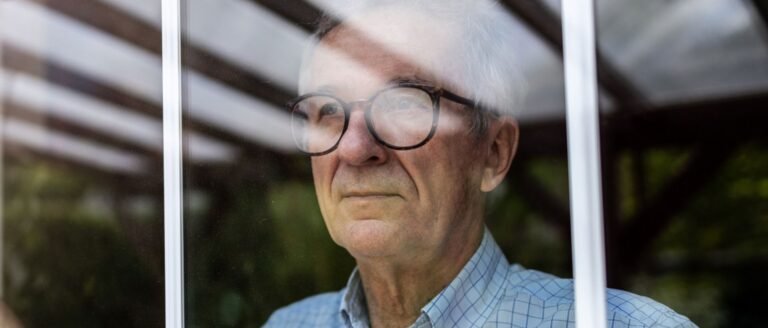 Homme âgé regardant pensivement par la fenêtre, symbole de la perte de rôle social à la retraite