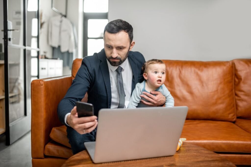 Manager débordé tentant de travailler avec son bébé sur les genoux, illustrant la difficulté à concilier charge professionnelle et vie personnelle.