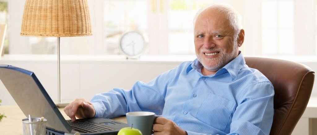 Homme retraité souriant travaillant sur ordinateur, symbolisant une utilité retrouvée et un nouveau rôle social après la retraite.