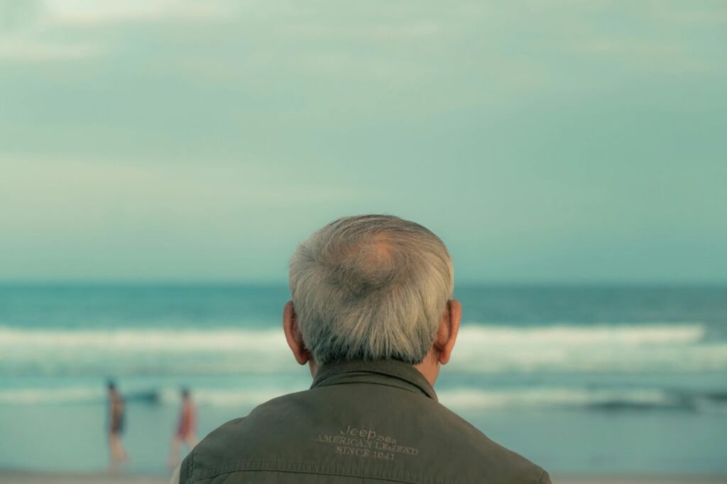 Homme senior assis face à la mer, regard perdu à l’horizon, symbolisant la perte de cap après la retraite.