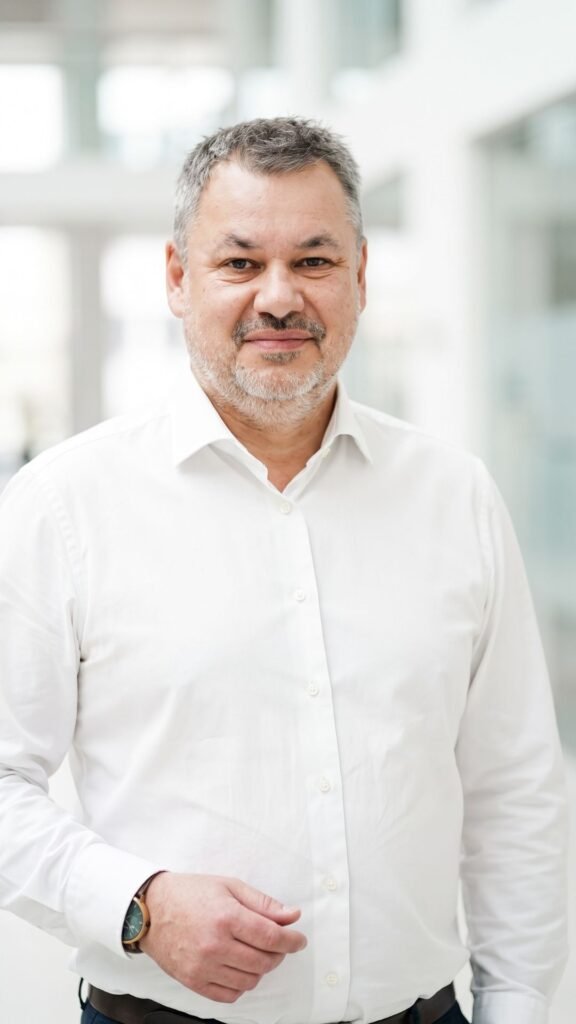 Portrait de Laurent de Vaucouleurs, Executive Coach certifié, souriant en chemise blanche dans un bureau lumineux. Expert en accompagnement stratégique pour les dirigeants de l'immobilier, de l'architecture et de la construction.
